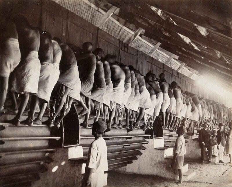Прикованные наручниками заключенные вращают ногами валы мельниц в тюрьме Янгуна (Мьянма). 1900 г.