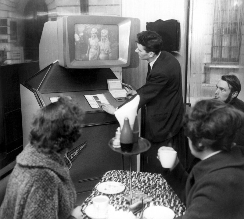 Люди вокруг музыкального автомата Scopitone, смотрят музыкальный клип. Париж, Франция, 1963 год
