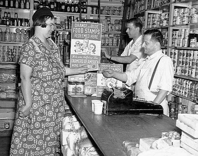 Женщина, которая делает покупки в местном продуктовом магазине, используя свои талоны на продуктовый паёк во время Второй мировой войны.
