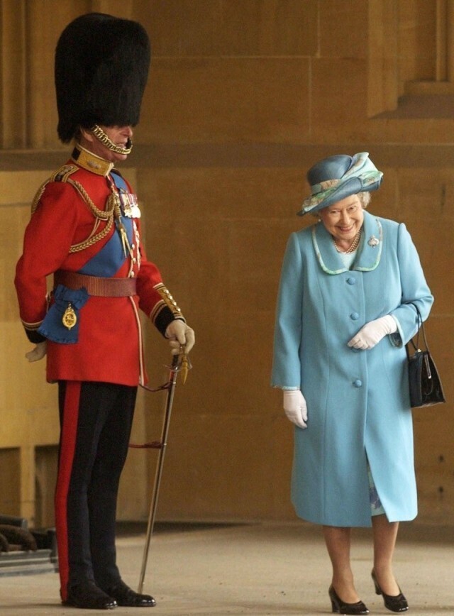 Королева пытается не засмеяться, проходя мимо своего супруга, герцога Эдинбургского, в шутку переодевшегося в гвардейца.
