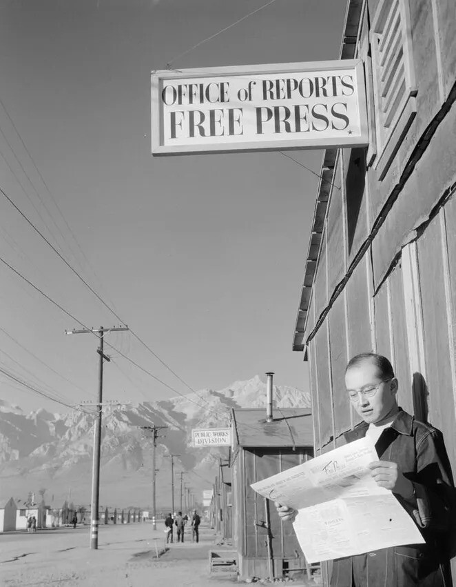 15. Редактор Рой Такено читает газету Manzanar Free Press перед редакцией газеты в военном центре переселения Манзанар.