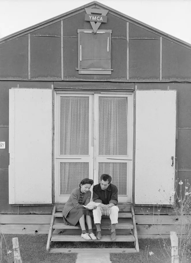 18. Мужчина и женщина читают письмо, сидя на деревянной лестнице перед зданием YMCA.