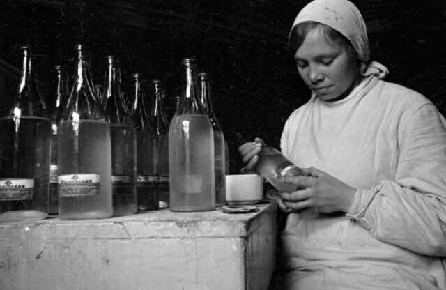 Работница водочного завода наклеивает этикетки на бутылки с водкой особой «Московской». 1930-е