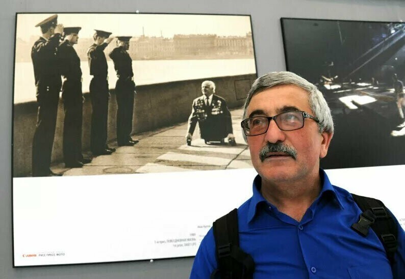 Фотограф Иван Куртов на выставке на фоне своей фотографии моряки отдают честь безногому ветерану