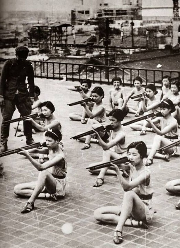 Японские школьницы, позируют для съемки на занятии по военной подготовке, где военный инструктор преподает им умение держать оружие правильно. 1930-е годы