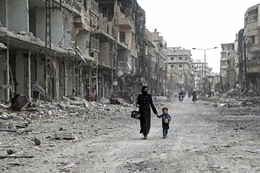 Сирийская женщина и ребенок идут по разрушенной улице, пока мирные жители и повстанцы готовятся к эвакуации.