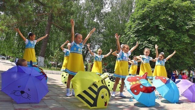 Девочки с зонтиками танцуют на празднике в парке.