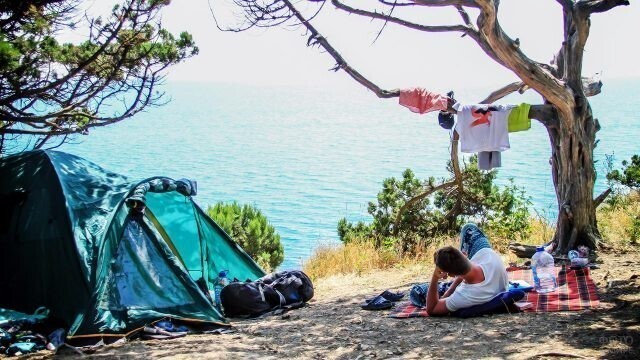Эко-турист отдыхает в тени у палатки с видом на море.
