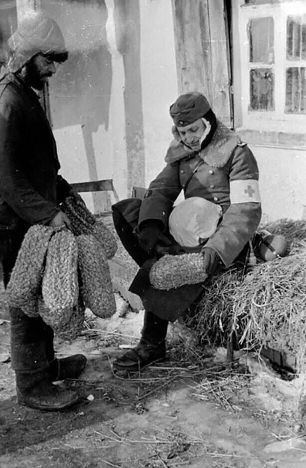 Фельдфебель немецкой санитарной службы примеряет соломенную обувь, сплетенную украинским крестьянином. Украина, февраль 1942 года