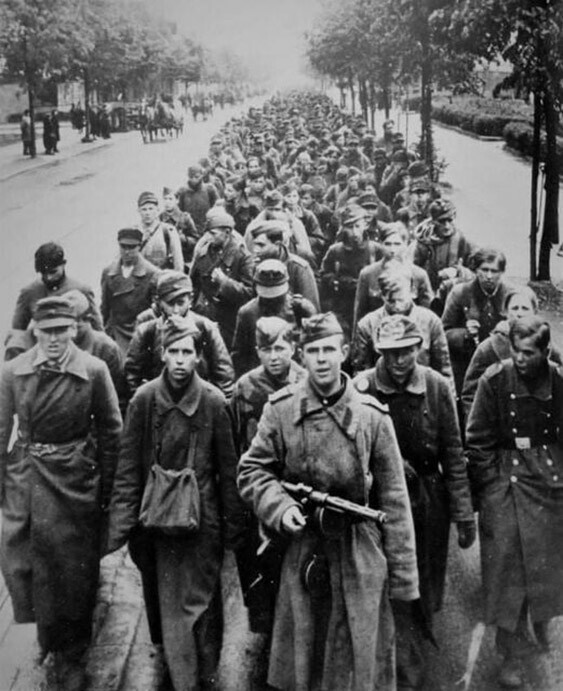 Сержант Красной Армии с пистолетом-пулеметом ППД ведет колонну немецких военнопленных по улице Берлина.  Снимок сделан в берлинском районе Райниккендорф (Berlin-Reinickendorf). Берлин, май 1945 год