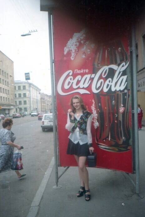 1. Девушка фотографируется на фоне уличной рекламы Coca-Cola, Россия, 1990-е