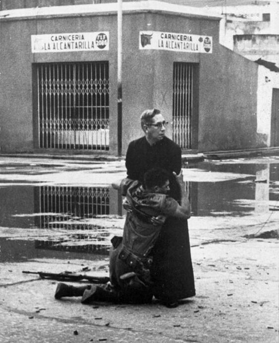 вященник держит в руках умирающего солдата, сраженного пулей снайпера. Автор - Эктор Рондон, священник - Луис Падильо, Венесуэла, 1962 год