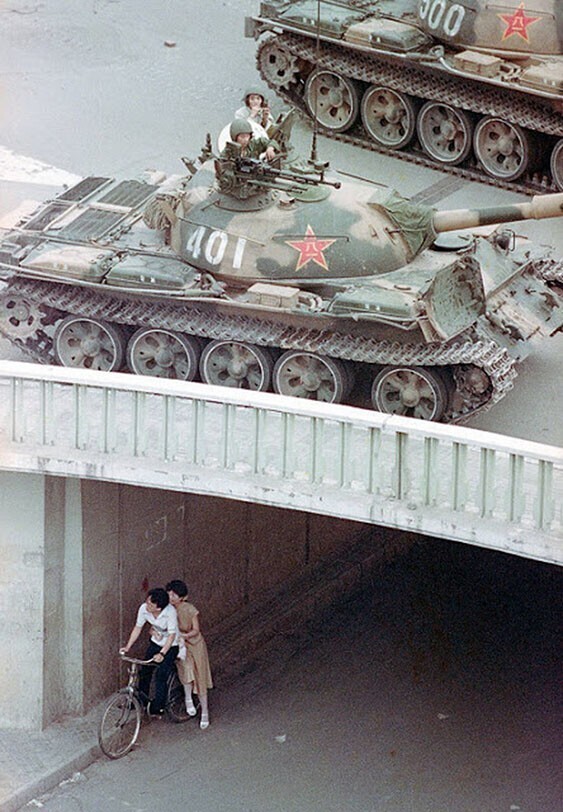 Китайская чета на велосипеде прячется под мостом от разворачивающихся в восточной части Пекина танков. 5 июня 1989 года