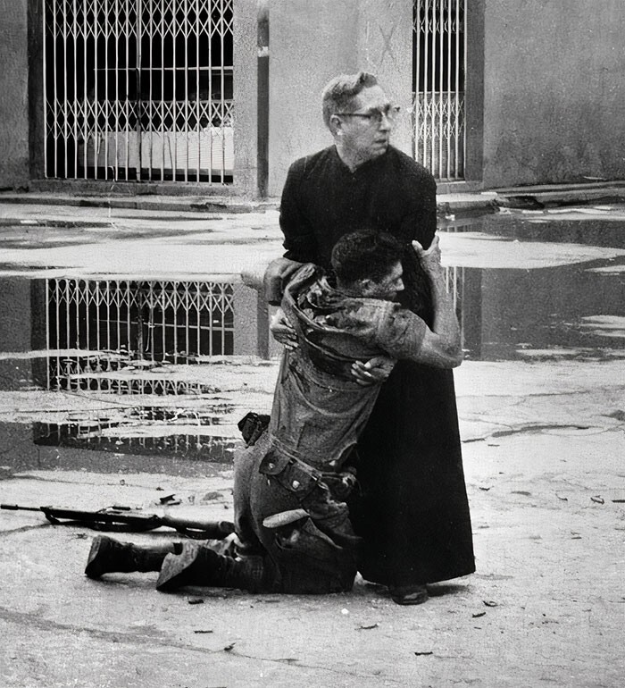 19. Отец Луис Мануэль Падилья держит раненого солдата, расстрелянного на улицах Пуэрто-Кабельо, Венесуэла во время восстания против президента Бетанкура в июне 1962 года