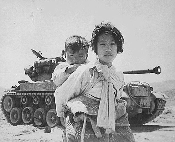 22. Со своим братом на спине измученная кореянка устало бредет мимо заглохшего танка М-26 в Хэнджу, Корея. 6 сентября 1951 года