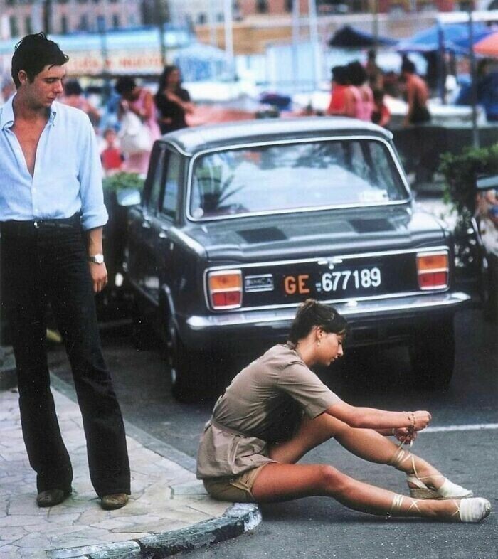 Мужчина остановился, чтобы посмотреть, как женщина завязывает сандалии в порту Портофино, август 1977 года
