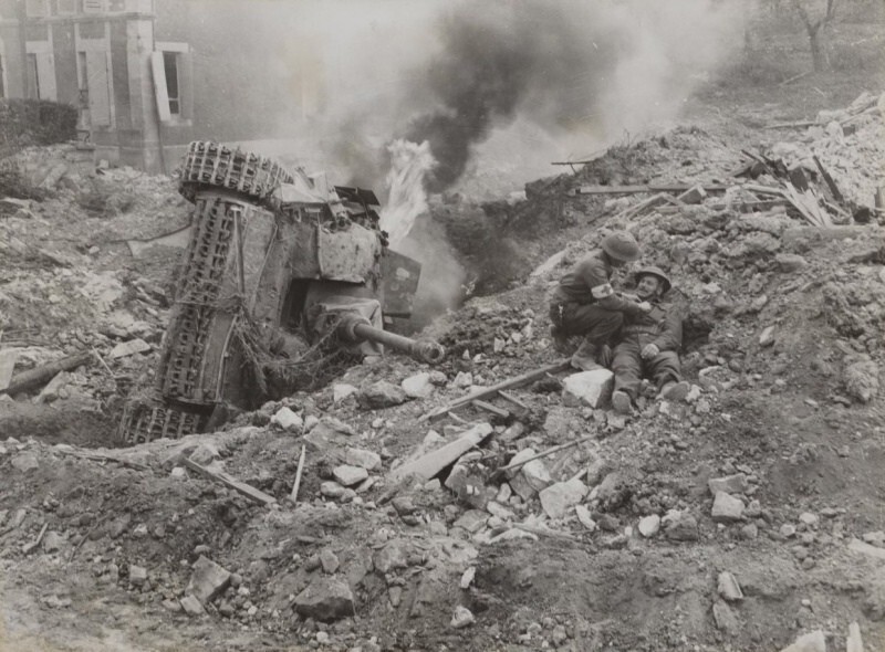 Канадский санитар оказывает помощь раненому у горящей немецкой САУ StuG III на улице разрушенного Фалеза (Falaise)