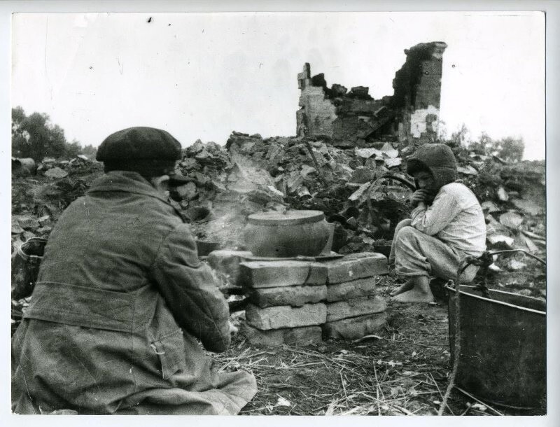 Коля и Леня Данилычевы готовят еду на пепелище своего дома. Деревня Средняя Гостомль Кромского района Орловской области. Август 1943-го года
