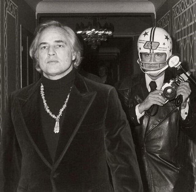 Папарацци Рон Галелла в футбольном шлеме пытается сфотографировать актёра Марлона Брандо. В предыдущий раз фотограф получил перелом челюсти и потерял пять зубов, после того как Брандо его ударил, 1973 год