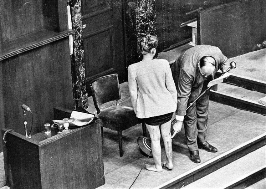 Бывшая узница нацистского концлагеря Равенсбрюк демонстрирует на Нюрнбергском процессе следы издевательств в присутствии дающего пояснения врача, 1946 год