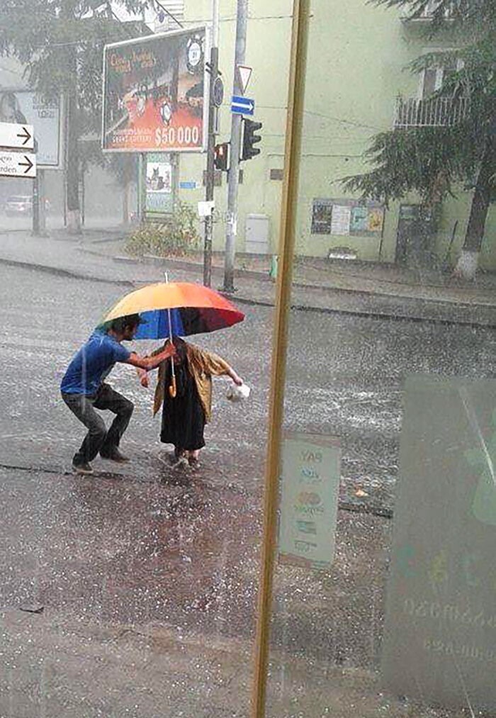 18. "Мужчина укрывает пожилую женщину зонтом от града"