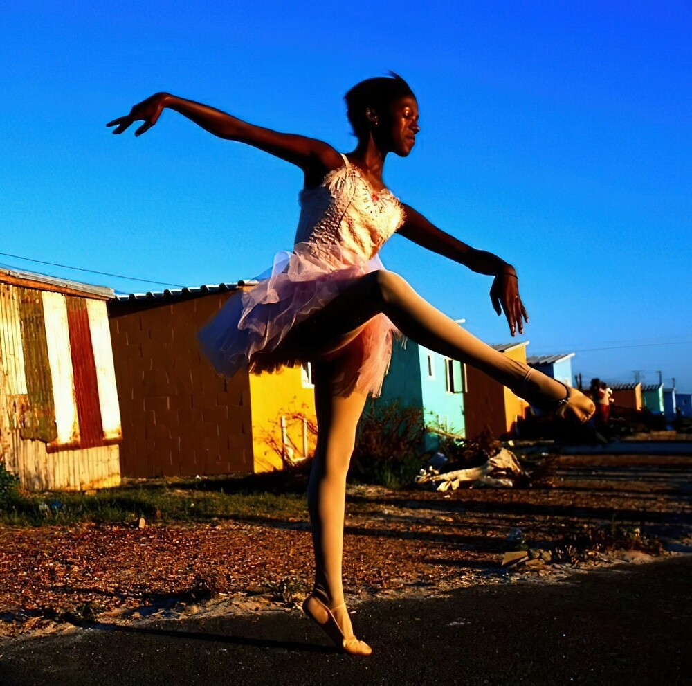 6. Нолуянда Мкутвана танцует возле двухкомнатной лачуги своей семьи в Хайелитше, одном из самых бедных черных поселков за пределами Кейптауна (Южная Африка, 2000 г.)