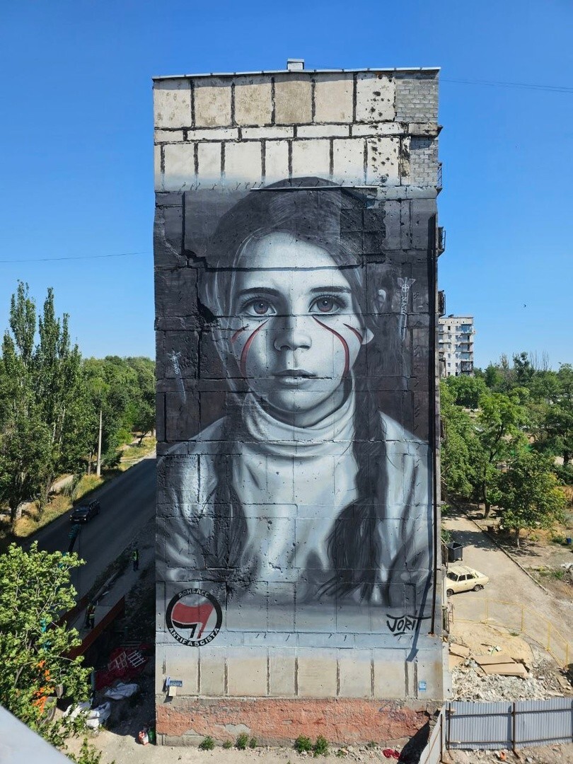 В Мариуполе появился посвященный детям Донбасса мурал в исполнении итальянского художника Йорита Черулло. На фасаде 9-этажного дома художник изобразил девочку Настю, позади которой падают бомбы НАТО