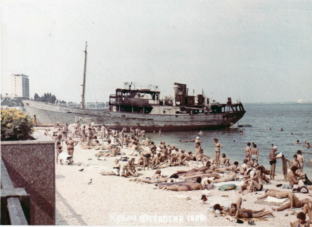 В Феодосии народ загорает на пляже на фоне ржавеющего баркаса СР-185