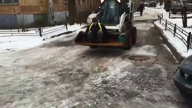 Дворник разбрасывает песок руками сидя в ковше