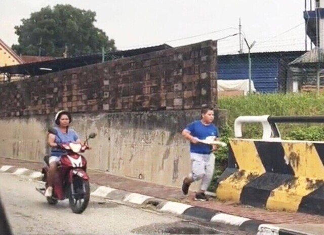 В Малайзии женщина на мотоцикле и с палкой в руках заставляет бегать своего полного сына