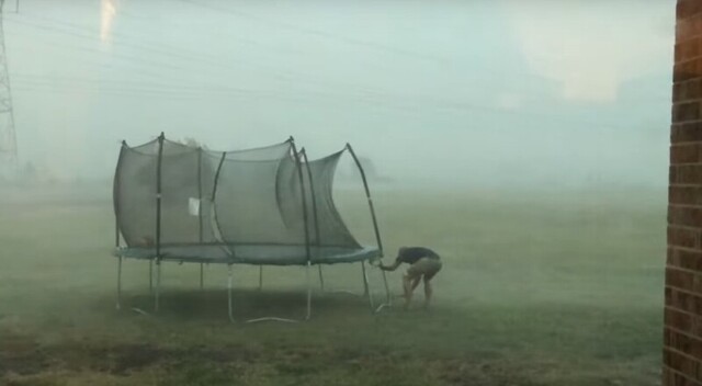 Мужчина пытается спасти батут во время шторма